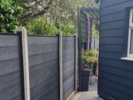 Dark grey composite fence panels in concrete posts along a side path beside a dark-clad building