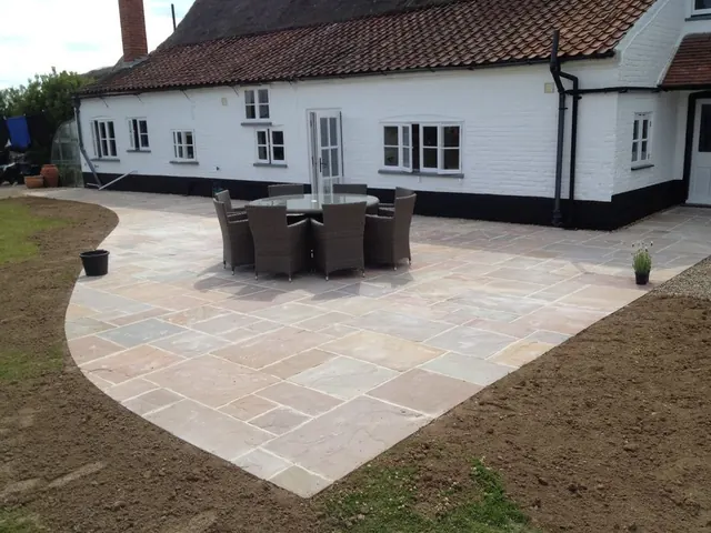 Sandstone patio with a curved edge and a rattan dining set outside a white-painted cottage with a pantile roof