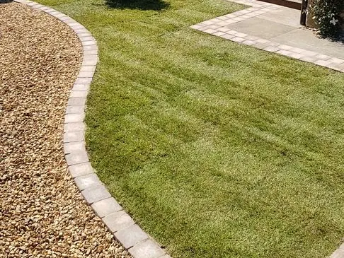 New turf lawn with a curved block-paved edge separating it from a golden gravel area
