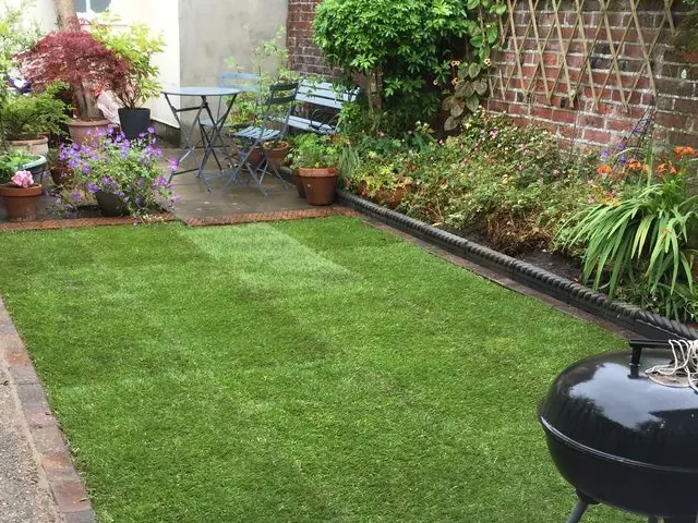 Freshly laid turf lawn with a block-paved edge in a cottage garden, with flower borders along a brick wall