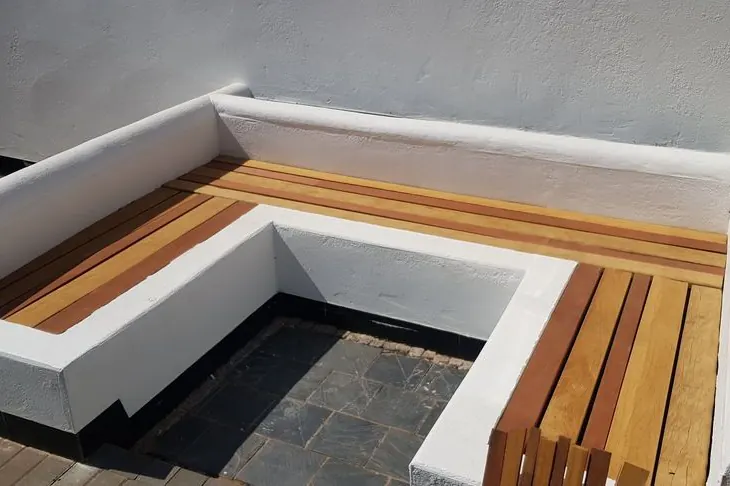 White rendered built-in garden seat with a hardwood slatted top wrapping round a sunken area paved in dark slate