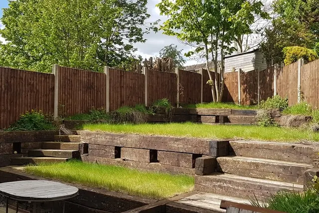 Sloping back garden terraced with reclaimed timber sleepers, with sleeper steps, two level lawns and a closeboard fence