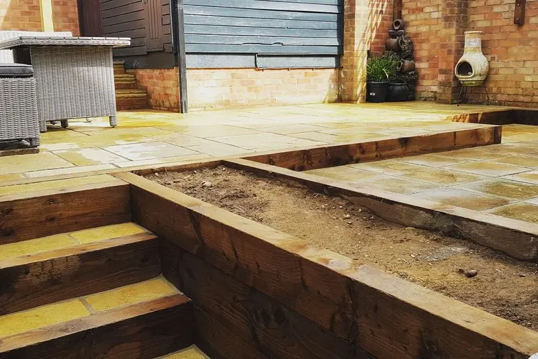 Sandstone patio on two levels joined by timber sleeper steps, with a sleeper raised bed filled with soil